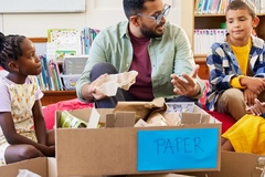 teacher shows children how to recycle paper