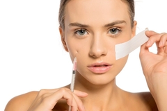Image A woman holding a needle and tape to her face.