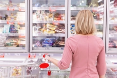 woman in pink sweater looking at frozen food section in supermarket