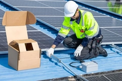 Image A person in a yellow vest and white helmet working on a solar panel