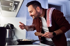 A man enjoying the aroma of his meal in a pan, cooking in his kitchen.