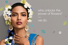 Image Woman wearing blue traditional attire adorned with white and blue flowers in her hair, statement gold jewelry, and soft glam makeup, with floral-themed branding text beside her.