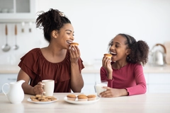 Image A mother and daughter eating cookies and smiling at a table in the kitchen.