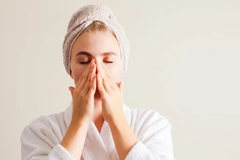 Image A woman with her hair in a towel and touching her face.