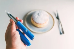 Image A person holding a GLP-1 medication injector in front of a donut.