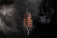 Image smoky meat pieces on fork against black background