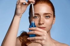 Image A woman holding a bottle of serum in front of her face.