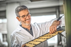 mature man in white lab coat pulling out tray of biscuits