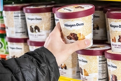 Image Human hand holding a pint of Haagen Dazs ice cream at a supermarket freezer.