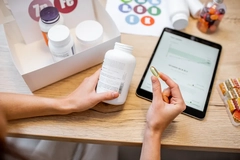 Hands holding supplement and package over pad on desk