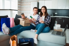 A couple opens items out of paper packaging on their couch.