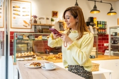 Image young woman taking photo of bakery item in cafe