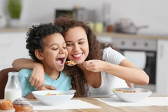 A young mother feeds her child some breakfast cereal at the kitchen table.