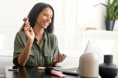 Image A woman putting makeup on in front of her computer.