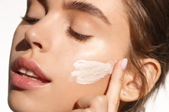 Image A woman swiping cream on her cheek.