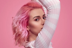 A woman with pink hair and her arms above her head.
