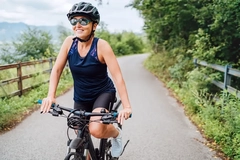 Image Portrait of a happy smiling woman dressed in cycling clothes, helmet and sunglasses riding a bicycle on the asphalt out-of-town bicycle path.