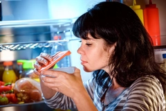 Image Woman opened the refrigerator and sniffs a container of food.