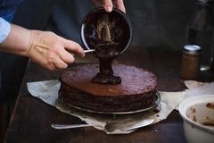 Image Chef's hand spreading chocolate ganache glazed over torte.