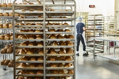 worker moving racks with croissants inside bakery