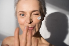 woman with white hair smiling at camera winking, cream on cheek