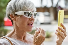 Image Older woman using her phone to apply lipstick