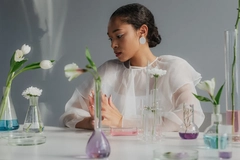 Image A woman with beakers and plants in front of her.