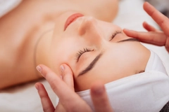 Image A woman with her eyes closed and a hair band on while hands touch her face.