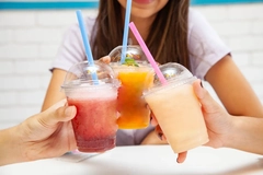 thrree teenagers' hands with colorful slushie drinks in plastic cups