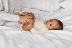 Image parent bending legs of baby on bed