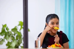 Image smiling girl snacking on paprika at table