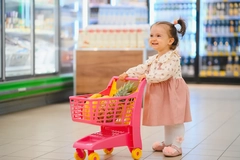 Happy baby girl shopping with toy cart in supermarket