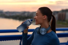 woman drinking water from a bottle outside while exercising
