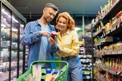 Man and woman in the grocery store with a trolley cart looking at food labels.
