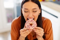 Image A woman eating a very sweet looking doughnut.