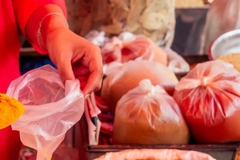 Image a person holding a plastic bag near several tied plastic bags filled with various powdered spices