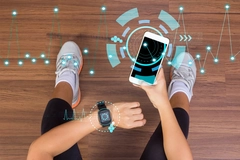 Image shot of sporty woman sitting on floor, looking at health watch and phone app