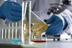 Image close up of researcher in lab coat wearing gloves holding a beaker oil oil