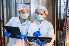 Image two scientists look at clipboard with safety gear on