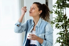 Image a woman enjoying a spoonful of yogurt indoors
