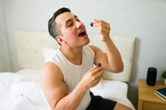 Image man in his bedroom, taking his daily supplement dose with a dropper