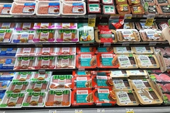 Image Grocery store refrigerator section with rows of various brands of plant based protein substitutes.