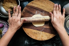 Indian women hand rolling wheat flour dough with rolling pin.