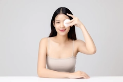 Image A woman holding a cotton pad in front of her face.
