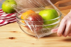 Image A person putting film over a bowl of fresh fruit
