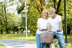An older couple hanging out and the man is about to ride a bike with a pretty nice wicker basket on it.