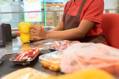 Image A supermarket cashier weighing or handling yellow produce at a checkout counter.