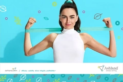 Image Woman in a white sleeveless top flexing her arms with a turquoise resistance band against a bright blue background featuring Ashland branding.