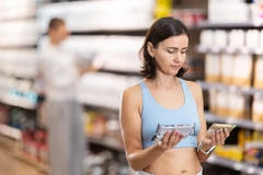A woman compares ingredients on two protein bars in a store. A woman compares ingredients on two protein bars in a store.