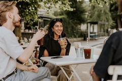 Image Three friends enjoy iced coffee and conversation at an outdoor café, with a smiling woman seated at the center